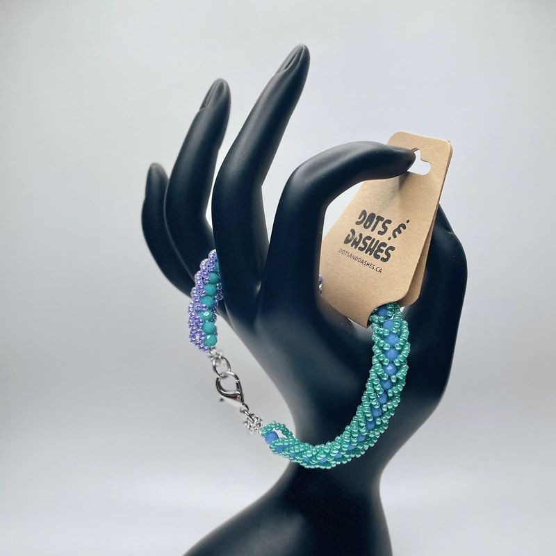 Picture of the Fuzzy caterpillar bracelet, turquoise and lavender beads with st steel clasp with a small hand holding bracelet